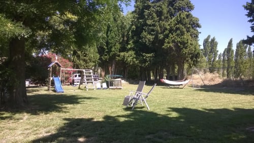 Spacious garden at Domaine Le Piboul with playground, loungers, and tall cypress trees lining the grounds in Fontcouverte