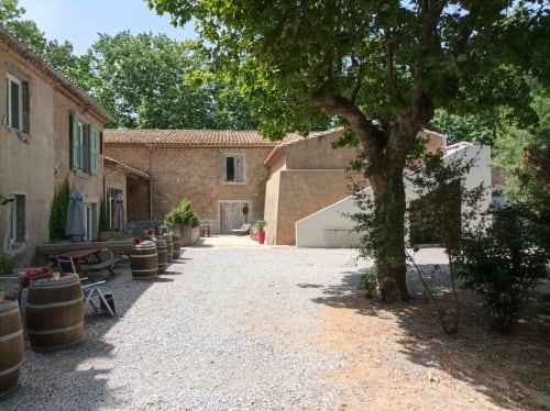 Rustic courtyard at Domaine Le Piboul in Fontcouverte with terracotta buildings, wine barrels, and shade trees