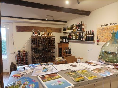 Wine tasting room at Domaine Le Piboul with bottles displayed on shelves and local maps on table in Fontcouverte
