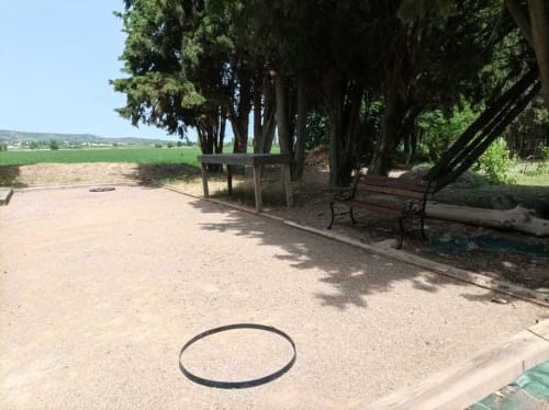 Rustic picnic area at Domaine Le Piboul with benches under tall trees overlooking green fields in Fontcouverte