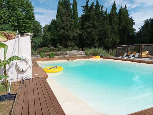 Turquoise pool with yellow kayak at Domaine Le Piboul, Fontcouverte, surrounded by cypress trees and wooden deck lounge area.