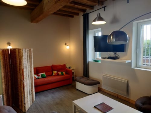 Modern lounge area at Domaine Le Piboul with red sofa, pendant lighting, exposed beams, and workspace in Fontcouverte