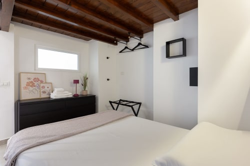 Camera moderna di LM Apartments Pavia con letto matrimoniale, cassettone nero, travi in legno e finestra con vista sulla città