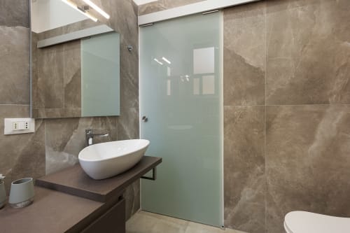 Bagno moderno dell'LM Apartments Pavia con lavabo ovale bianco, box doccia in vetro satinato e pareti in piastrelle color tortora