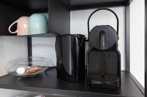 Mensola nera in cucina presso LM Apartments Pavia con macchina da espresso, bollitore elettrico e tazze colorate