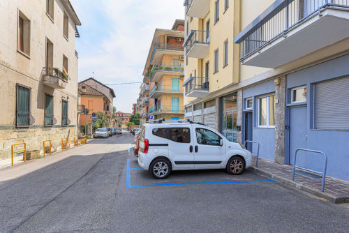 Furgone bianco parcheggiato in posto blu designato a Pavia, Italia vicino LM Apartments con edifici colorati