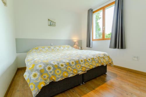Chambre lumineuse avec parure de lit motif tournesol, vue sur le jardin et plancher en bois aux gîtes Clubhouse