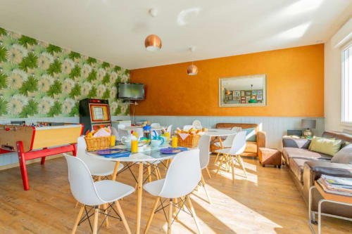Lumineux appartement deux chambres aux Clubhouse Gîtes avec salle à manger, mur d'accent orange et mobilier moderne avec vue