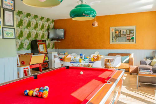 Salle de jeux colorée au Clubhouse Gîtes avec billard rouge, murs orange, luminaire vert et coin repas à Beussent.