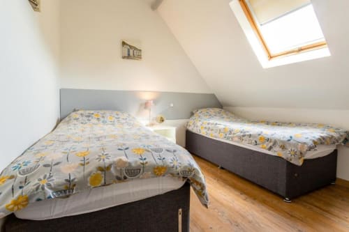 Chambre lumineuse sous les combles avec deux lits jumeaux à draps fleuris, parquet et velux au gîte de Beussent