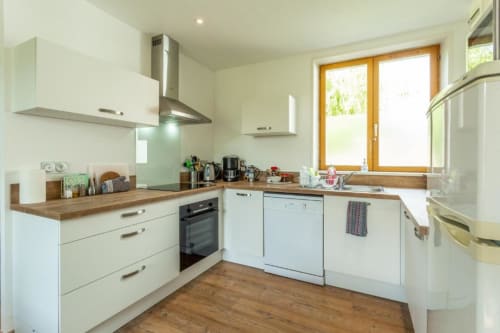 Cuisine moderne avec armoires blanches, plans de travail en bois et vue sur le jardin de l'appartement Clubhouse Gîtes à Beussent, France