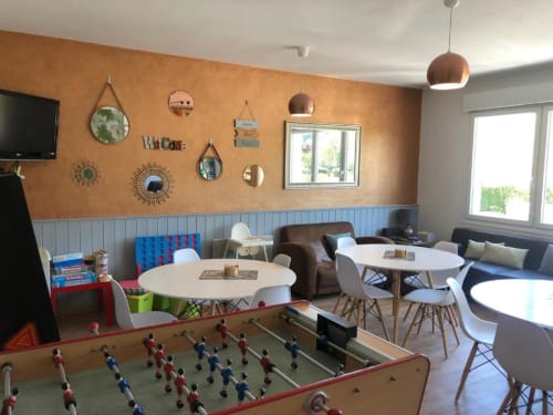 Salon familial du Clubhouse Gîtes avec baby-foot, tables rondes, mur en terre cuite, et