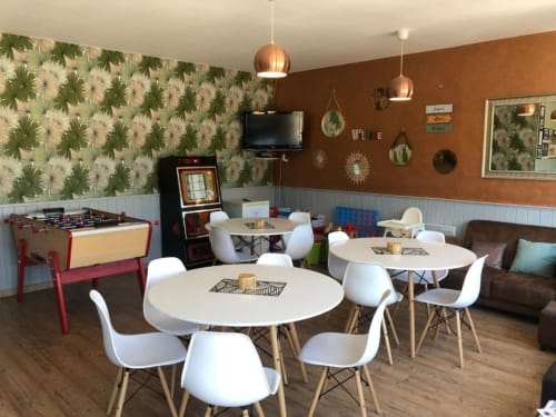 Espace commun du Clubhouse Gîtes avec tables blanches rondes, baby-foot, télévision et décoration avec vue sur le jardin à Beussent.