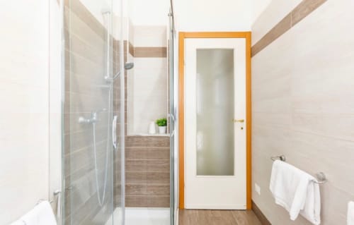 Bagno moderno negli appartamenti in affitto breve LM Apartments Pavia, con cabina doccia in vetro, piastrelle bianche e