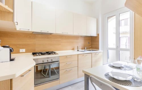 Cucina moderna negli Appartamenti LM Pavia con mobili in legno chiaro, pensili bianchi, fornello a gas e zona pranzo con vista sulla città