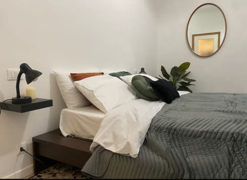 Camera moderna di LM Apartments Pavia con trapunta grigia, cuscini bianchi, lampada da scrivania nera e pianta verde