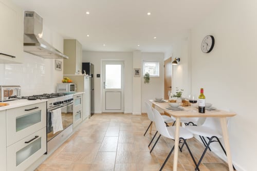 Modern kitchen-diner in Stevenage villa with white cabinetry, stainless steel appliances, wooden table, and garden view