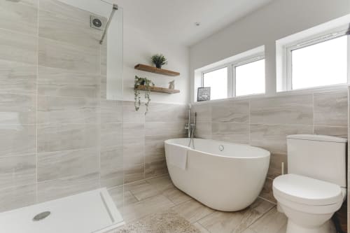 Modern bathroom at Towerserve Properties villa in Stevenage with freestanding tub, walk-in shower, and wooden shelving