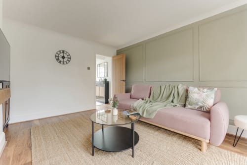 Modern pink sofa in light-filled Stevenage villa living room with wooden flooring and garden view