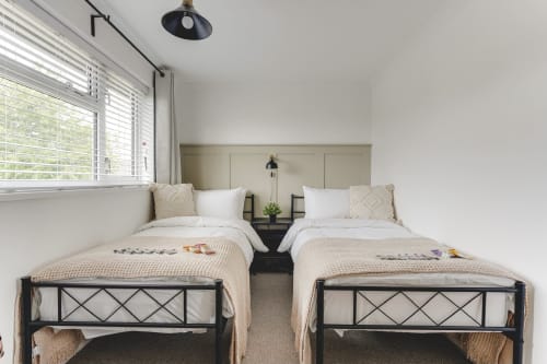 Twin beds in modern Stevenage villa with garden views, black frames, white linens, neutral decor, and pendant lighting.