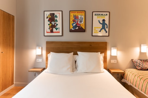 Chambre d'hôtel moderne au Louvre Richelieu Paris avec lit en bois, linge blanc, affiches vintage et éclairage ambiant