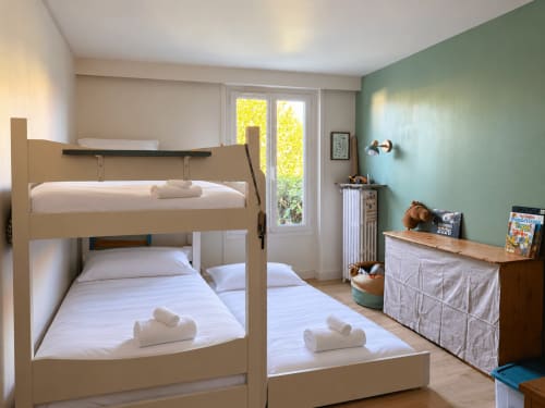 Chambre d'enfants lumineuse à la villa ARLOÉ à La Rochelle avec lits superposés, draps blancs, mur d'accent vert et vue sur le jardin
