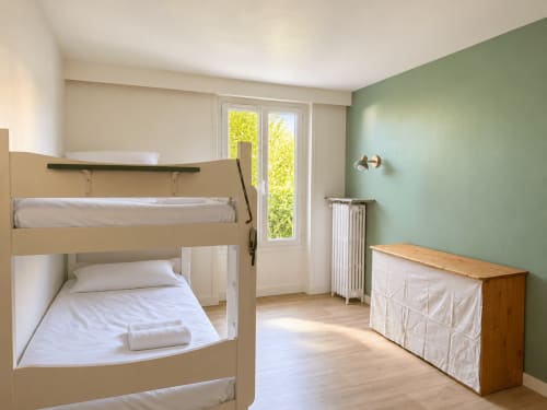 Chambre lumineuse de la villa ARLOÉ La Rochelle avec lits superposés, mur d'accent vert et vue sur le jardin par les portes-fenêtres
