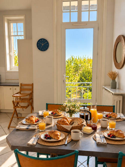 Petit-déjeuner lumineux à la villa ARLOÉ à La Rochelle avec croissants, fruits frais, jus d'orange et vue sur le jardin