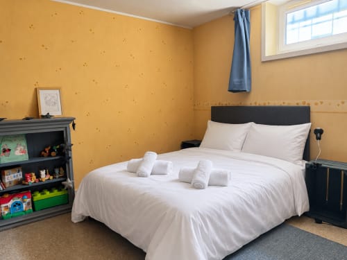 Chambre jaune éclatante à la villa ARLOÉ à La Rochelle avec lit blanc, serviettes roulées et vue sur le jardin