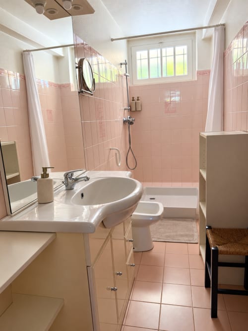 Salle de bains moderne aux carrelages rose, lavabo sur pied, douche vitrée et vue sur le jardin de la villa ARLOÉ à La Rochelle