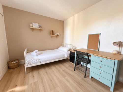 Chambre élégante à la villa ARLOÉ avec lit blanc, commode turquoise, bureau en bois et vue sur le jardin à La Rochelle