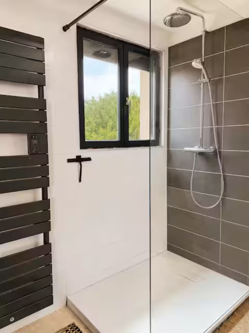 Salle de bains moderne à la Villa Alba ARLOÉ avec douche pluie, radiateur noir, vue sur jardin et carrelage gris