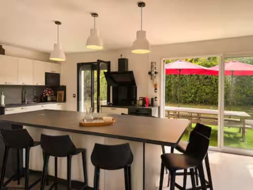 Cuisine ouverte et salle à manger Villa Alba avec tabourets noirs, suspensions luminaires et vue sur le jardin à ARLOÉ, La Rochelle