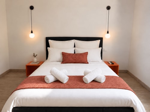 Chambre moderne à la villa ARLOÉ à La Rochelle avec tête de lit noire, draps blancs, jetée de lit rouille et luminaires suspendus