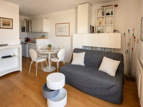 Salon moderne à La Rochelle avec canapé gris, table à manger, cuisine et rangements blancs