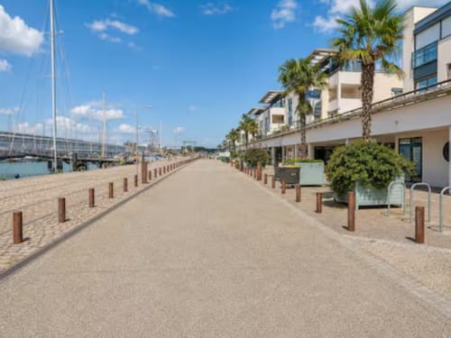 Promenade en bord de mer de l'hôtel ARLOÉ à La Rochelle avec allée sablée, palmiers, appartements modernes et vue sur le pont du port