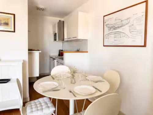 Salle à manger avec table ronde et chaises crème dans l'appartement ARLOÉ à La Rochelle, cuisine ouverte et décoration nautique visible