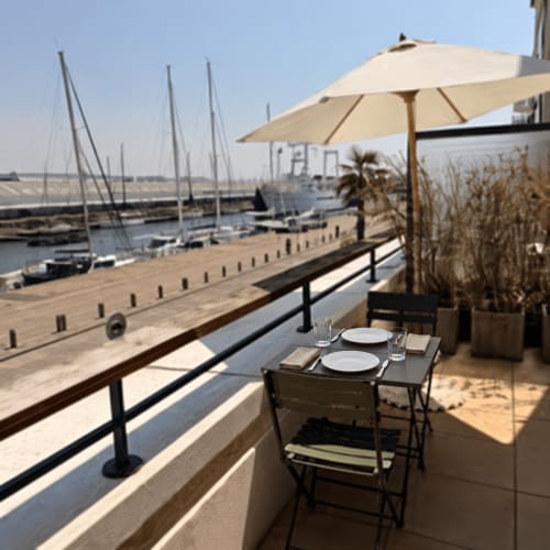 Espace de repas en bord de mer à l'appartement ARLOÉ à La Rochelle avec vue sur les voiliers et la marina sous parasol crème