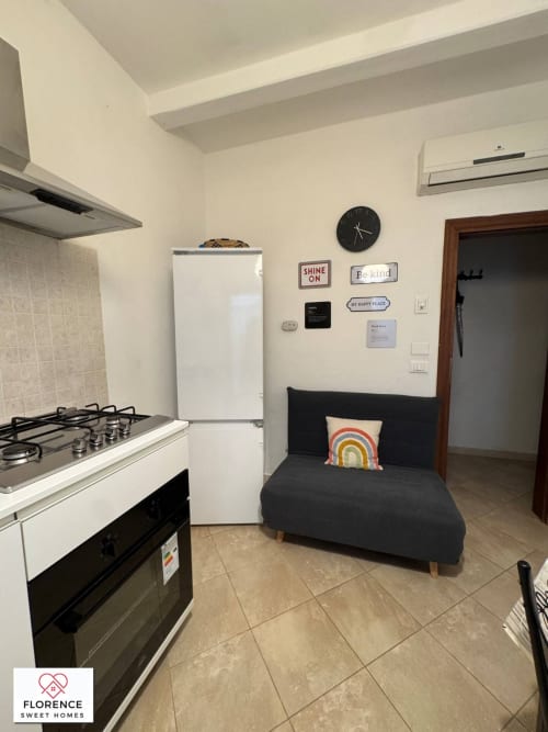 Zona cucina-soggiorno moderna nell'appartamento Florence Sweet Homes con fornello, frigorifero, divano nero e decorazioni a parete