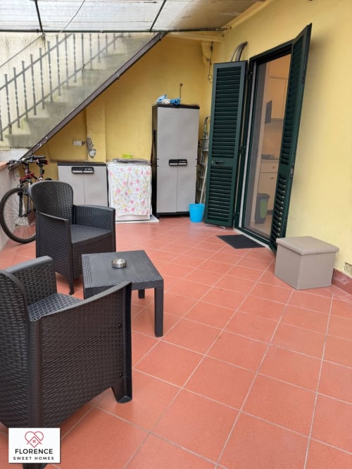 Terrazza coperta con sedie in vimini nero, pavimento in cotto rosso e porte con persiane verdi a Florence Sweet Homes