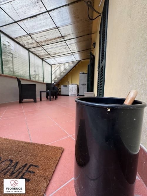 Terrazza coperta con pavimento in piastrelle rosse, cestino nero, arredi esterni e parete gialla dell'edificio a Florence Sweet Homes
