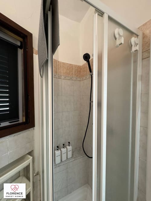 Moderno box doccia in appartamento fiorentino con soffione nero, piastrelle bianche in stile metro e flaconi di cortesia