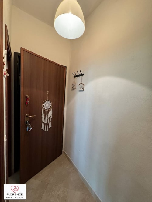 Ingresso luminoso dell'appartamento La casa di Mary a Firenze con porta in legno, acchiappasogni e lampada moderna al soffitto