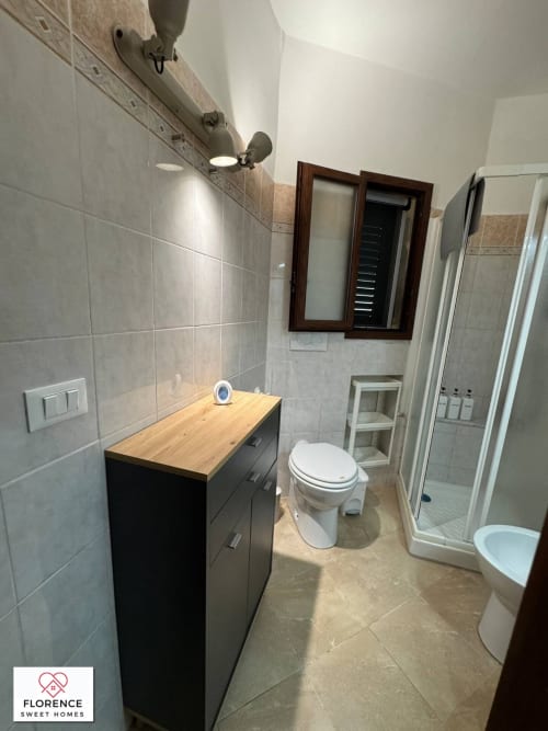 Bagno moderno nell'appartamento Florence Sweet Homes con vanità nera, piano in legno, WC e cabina doccia in vetro