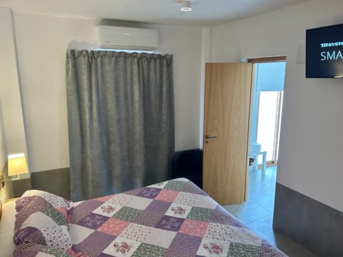 Habitación doble en Hostal Fornet Altea con cama de colcha patchwork, aire acondicionado, cortina divisoria y puerta de entrada de madera.