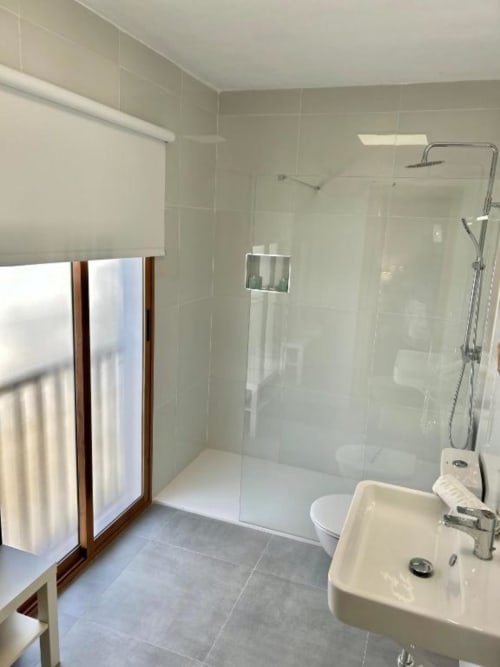 Baño moderno del Hostal Fornet Altea con ducha a ras de suelo, lavabo blanco, inodoro y piso de cerámica