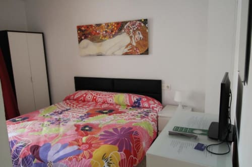 Habitación triple colorida en Hostal Fornet Altea con ropa de cama vibrante, escritorio, cabecero negro y arte con vista a montaña.