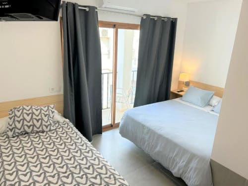 Habitación triple en Hostal Fornet Altea con dos camas, cortinas oscuras, acceso a balcón y servicios modernos en Altea, España.