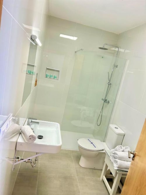 Baño moderno con ducha de cristal, inodoro y lavabo en el Hostal Fornet Altea de España