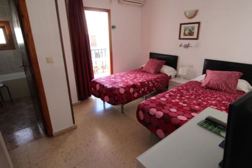 Habitación doble en Hostal Fornet Altea con ropa de cama de lunares burdeos, paredes rosa y acceso a balcón